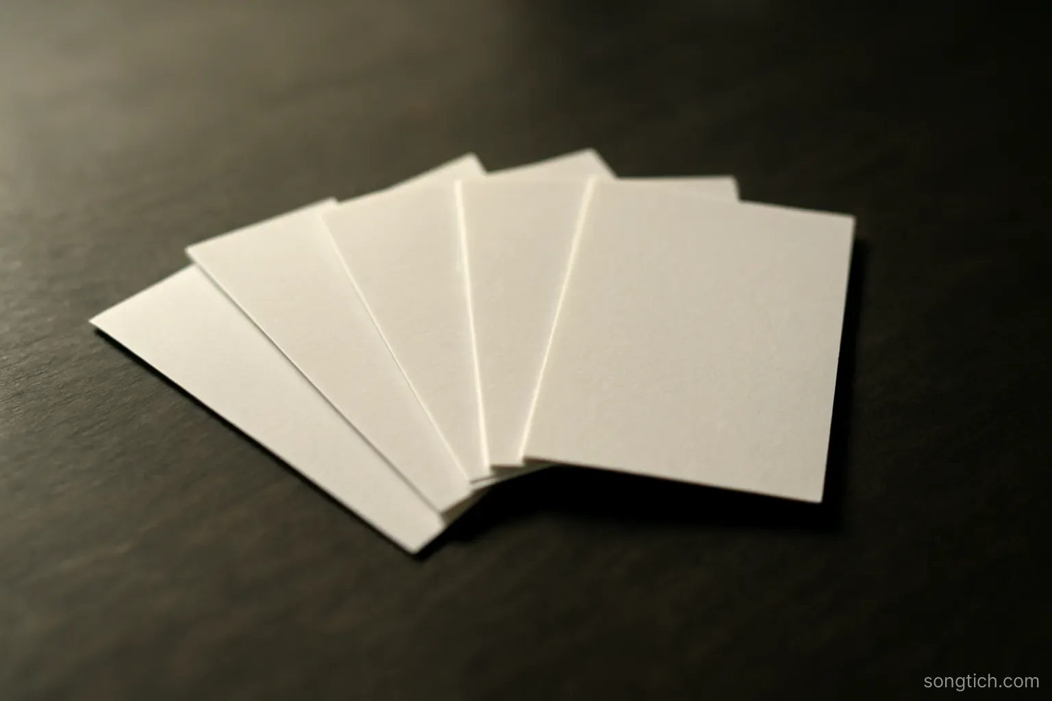 five small blank paper slips arranged in a loose fan on a dark tabletop, lit from one side